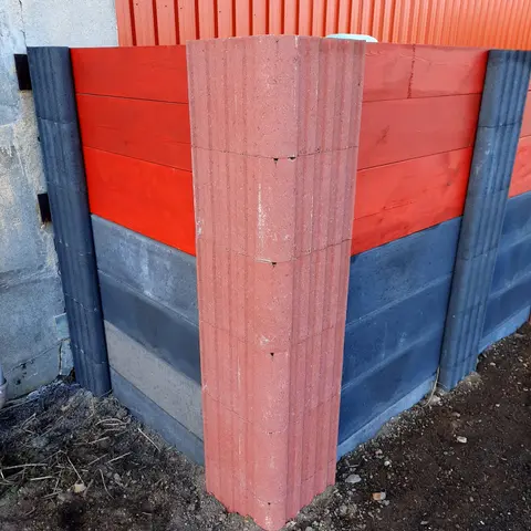 Ecke einer Sichtschutzwand mit rotem Vablo Eckpfosten, unten anthrazitfarbene Betonriegel, oben rot gestrichene Holzbohlen