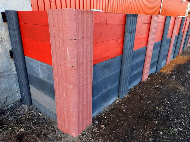 Sichtschutzwand mit rotem Vablo Eckpfosten im Vordergrund: unten anthrazitfarbene Betonriegel, oben rot gestrichene Holzbohlen