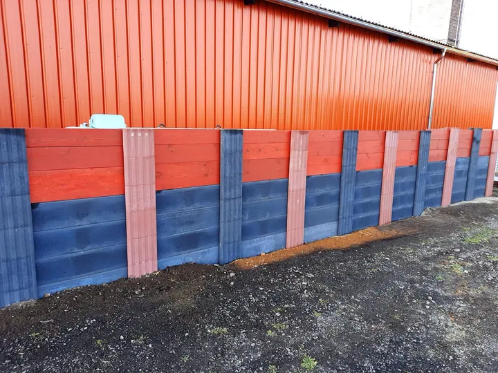 Sichtschutzwand aus roten und anthrazitfarbenen Vablo Pfosten, unten anthrazitfarbene Betonriegel, oben rot gestrichene Holzbohlen