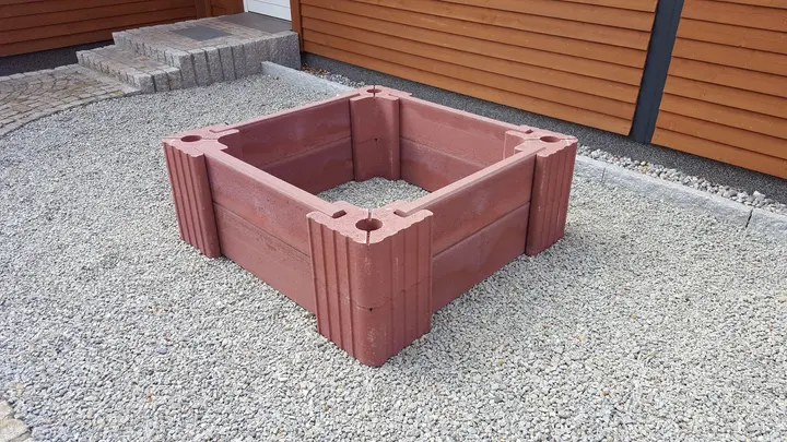 Quadratisches Hochbeet aus roten Vablo Ecksteinen und Betonriegeln in zwei Lagen, schräg von vorn auf Kies