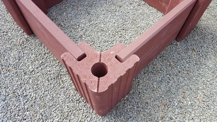 Blick von oben auf eine Hochbeet-Ecke: roter Vablo Eckstein mit Mittelloch, in dessen Aufnahmen zwei Betonriegel stecken