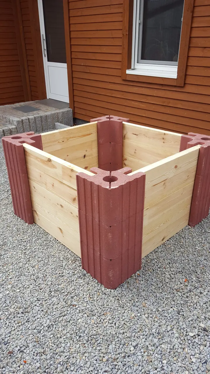 Hohes quadratisches Hochbeet aus drei Lagen roter Vablo Ecksteine mit hellen Holzriegeln, schräg von oben auf eine Ecke mit Mittelloch