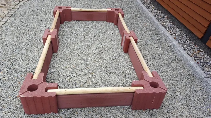 Lange niedrige Beeteinfassung aus roten Vablo Ecksteinen, Mittelsteinen und Betonriegeln mit Rundholzabschluss, schräg von oben