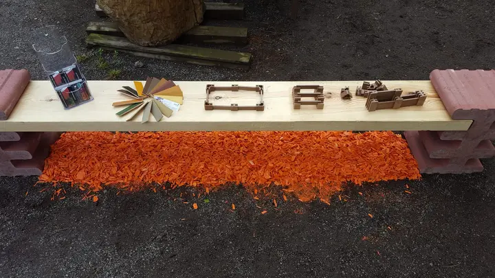 Bank aus Holzbohle und roten Vablo Steinen, auf der Sitzfläche kleine Modelle von Beeten und Mauern sowie ein Farbfächer