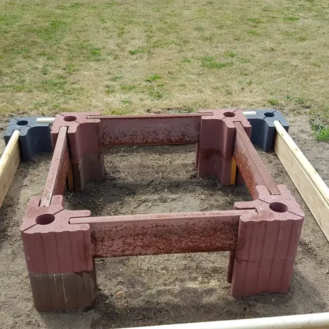 Aufbau eines Stufenbeets auf Sand: innen ein Rahmen aus gestapelten roten Vablo Ecksteinen mit Betonriegeln, außen ein niedriger Rahmen aus anthrazitfarbenen Ecksteinen mit Holzriegeln