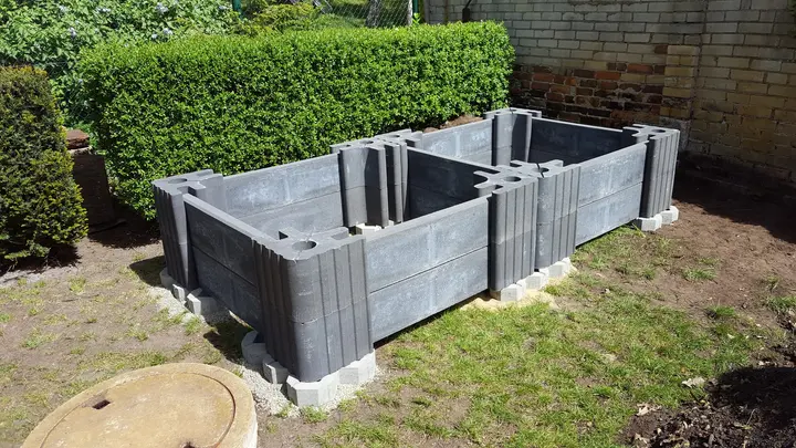 Doppel-Hochbeet aus grauen Vablo-Steinen mit Ecksäulen, Mittelstützen und eingeschobenen Riegeln, frisch aufgebaut im Garten.