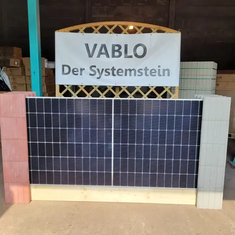 Solarmodul als Wandelement zwischen einem roten und einem hellgrauen Vablo Pfosten, dahinter ein Schild mit der Aufschrift „Vablo Der Systemstein“