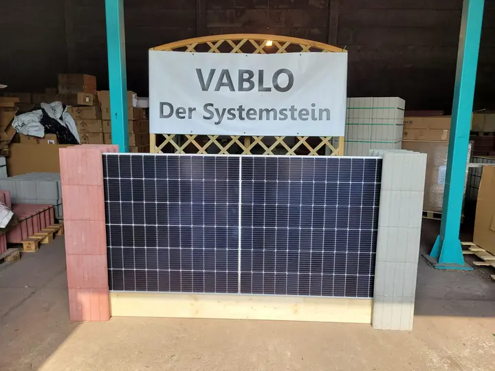 Solarmodul als Wandelement zwischen einem roten und einem hellgrauen Vablo Pfosten, dahinter ein Schild mit der Aufschrift „Vablo Der Systemstein“