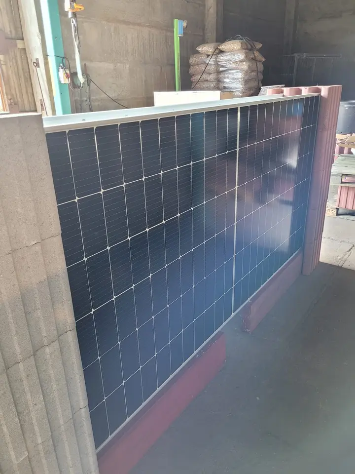 Schrägansicht eines Solarmoduls zwischen einem hellgrauen und einem roten Vablo Pfosten, unten eine rote Holzbohle