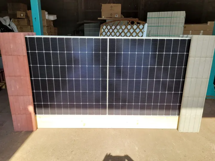 Senkrechtes Solarmodul auf einer Holzbohle, seitlich gehalten von einem roten und einem hellgrauen profilierten Vablo Pfosten, in einer Halle