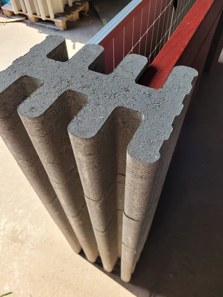Draufsicht auf einen grauen profilierten Vablo Pfostenstein mit mehreren Nuten, in denen ein Solarmodul und eine rote Holzbohle stecken